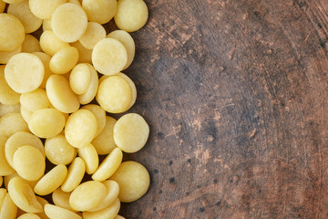 Organic cacao butter buttons (wafers) in wooden spoon on rustic background. Top view with copy space