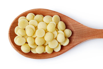 Organic cacao butter buttons (wafers) in wooden spoon isolated on white background. Top view