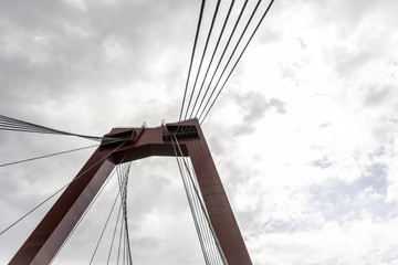 Naklejka premium Red pylon and cables of Willemsbrug bridge against cloudy sky. It is a cable-stayed bridge in the center of Rotterdam, spanning the Nieuwe Maas river and named after King Willem III of the Netherlands