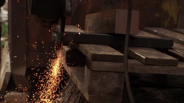 The manual machine for metal cutting works. Sparks fly to the parties. Working process of cutting of metal. The worker saws a detail. Quickly the disk rotates, bright sparks are scattered in the parti