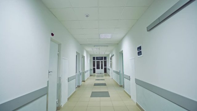 Walking slowly down a corridor hospital hall way with tiled floor and doors leading off on either side with white walls and ceiling