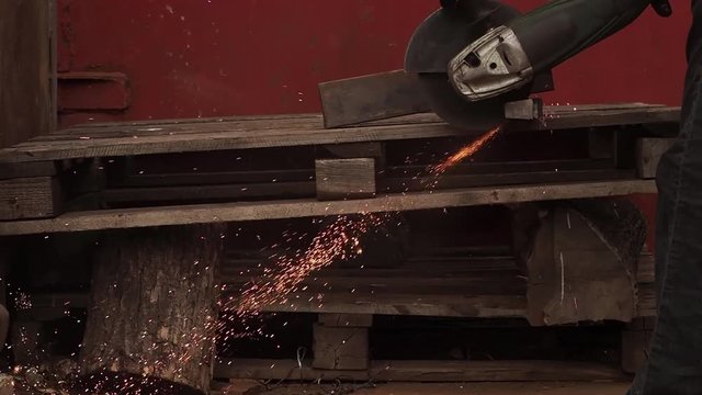 The manual machine for metal cutting works. Sparks fly to the parties. Working process of cutting of metal. The worker saws a detail. Quickly the disk rotates, bright sparks are scattered in the parti