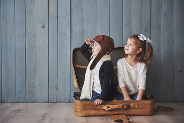 Happy kid in pilot hat and little girl playing with old suitcase. Childhood. Fantasy, imagination. Travel concept
