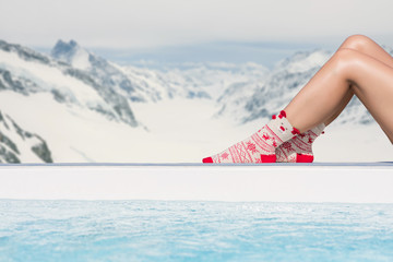 Women's feet in Christmas socks near the pool on the Swiss Alps background. Winter concept.