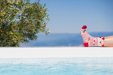 Women's feet in Christmas socks near the pool on the Olive tree and mountain background. Greece