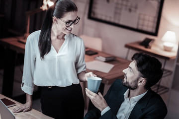 Friendly talk. Surprised man turning head to his colleague and stretching hand while taking tea