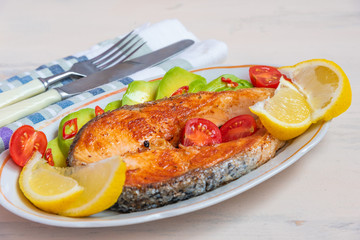 Grilled salmon steak with lemon, avocado, tomatoes on a plate close-up