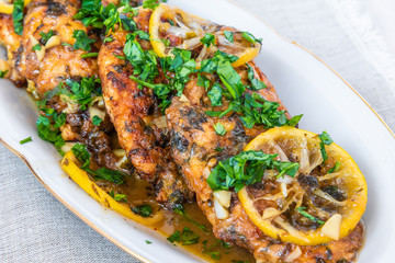 Chicken francese - fried chicken breast with lemon slices and delicious sauce on a white plate close-up, top view