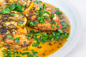 Chicken francese - fried chicken breast with lemon slices and delicious sauce on a white plate close-up, top view