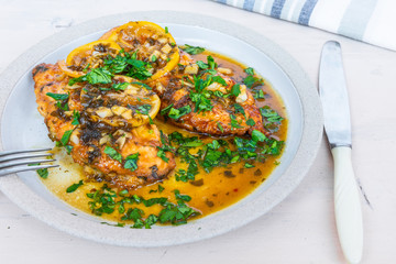 Chicken francese - fried chicken breast with lemon slices and delicious sauce on a white plate close-up, top view