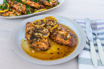 Chicken francese - Fried chicken breast with lemon slices and delicious sauce on a white plate on the table with a napkin, fork and knife, top view