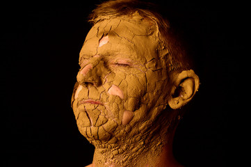 Face closeup portrait on black background. Dried clay on the face, cracked skin. Display of empty...