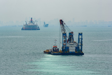 Fototapeta premium Grab Dredger - revolving crane, fitted with a grab, placed on a hopper vessel or pontoon. Singapore Strait.