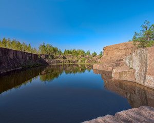 Fototapeta na wymiar Blue pond formed at the bottom of the abandoned granite quarry.