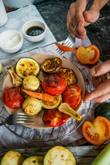 Healthy and healthy food: grilled vegetables and men's hand with fork in the frame, zucchini, eggplant, tomato, onion cooked on fire, on a dark background