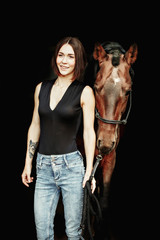 Portrait of smiling pretty woman standing by horse on the black background. Isolate
