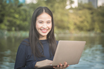 Young Asian woman using laptop on garden outdoor background.Happy freelancer working in the garden. Writing, surfing in the internet.