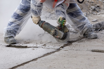 worker catching and using electric cutting machine tool to cut concrete floor with dirty dust spreading in air,