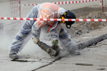 worker catching and using electric cutting machine tool to cut concrete floor with dirty dust spreading in air,