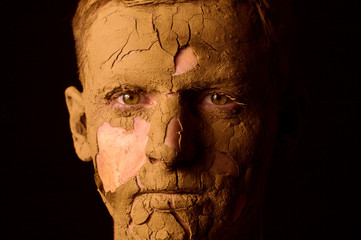 Face closeup portrait on black background. Dried clay on the face, cracked skin. Display of empty...