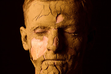 Face closeup portrait on black background. Dried clay on the face, cracked skin. Display of empty...
