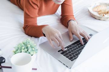 Charming young woman lying on bed and working with laptop.Morning coffee concept