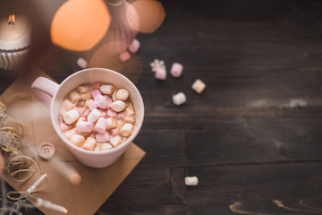 Mug of hot cocoa or hot chocolate with marshmallow and lights bokeh on wooden background
