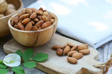 Almond nut in wooden bowl on wood table with green leaf background, copy space