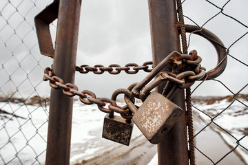 Gate locked with chain and several padlocks. Pair of rusty locks on metal chain. No trespassing,...