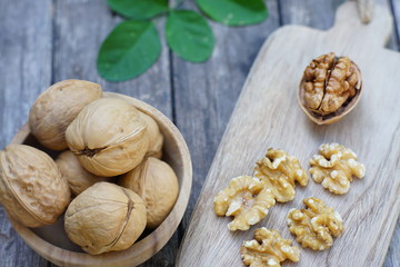 Walnut nut in wooden bowl on wood table with green leaf background, copy space