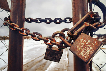 Gate is locked with  chain and several padlocks. Pair of rusty locks on a chain. Hazardous waste...