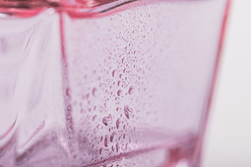 White and pink background. Glass with water drops. Perfume