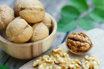 Walnut nut in wooden bowl on wood table with green leaf background, copy space