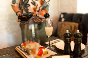 Girl pours champagne into glass in cozy cafe