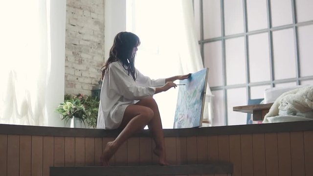 girl painter works in a home studio. the artist paints a picture sitting on the floor at home