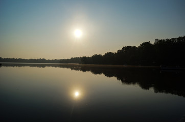 Fototapeta premium Sonnenaufgang spiegelt sich im See vor anwachsender Baumkette