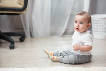 A little girl sitting on a laminate flooring in a bright room, happy