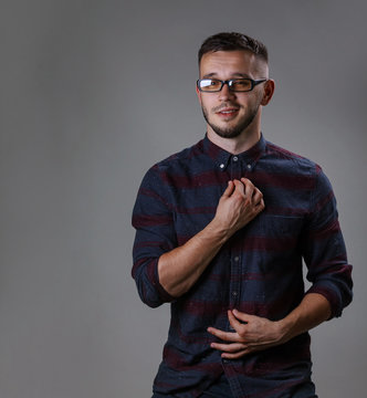 Attractive male wearing checkered shirt and strong black plastic glasses for low eyesight while stands on a dark gray background