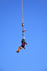 Bungee jumping. Beautiful young girl with long ponytail hanging on a cord high in the blue sky