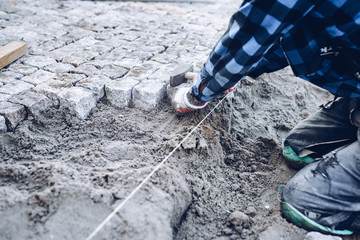 industrial worker installing pavement rocks, cobblestone blocks on road pavement