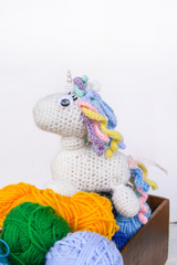 Handmade crocheted unicorn toy and yarn in a wooden box on white background.