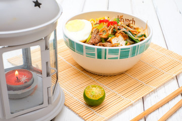 Malay Mee Rebus in the bowl  with chopsticks on white table This dish is made of noodles ,vegetable,egg with a spicy .
