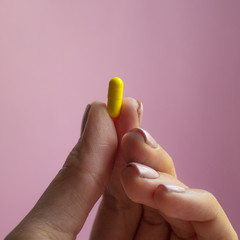 woman hand holding yellow pill capsule on pink background, medication concept with copy space