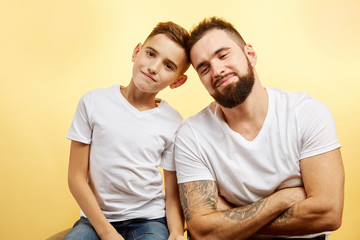 dad and son looking at camera on yellow background