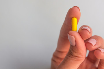 woman hand holding yellow pill capsule on light blue background, medication concept with copy space