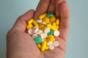 a lot of colorful pills in a woman's palm on ight background, medication concept