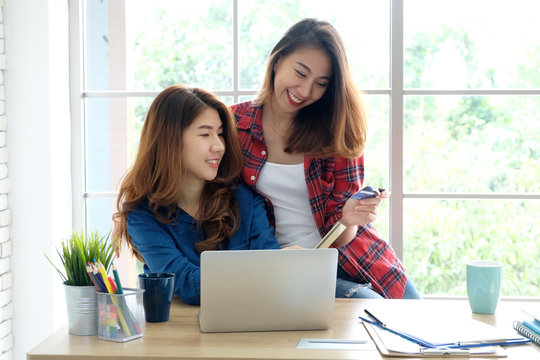  Two young asian women holding credit card and using laptop computer for shopping on line with happiness, business and technology concept, digital marketing, casual lifestyle