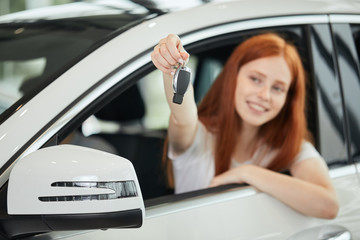 Cute content housewife with ginger hair in a white car shows car key in her hand and looking at...
