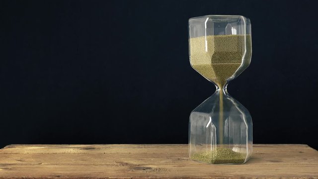 a hourglass on a wooden underground with black background