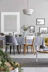 Lamp above chairs and table in grey dining room interior with mockup and posters. Real photo